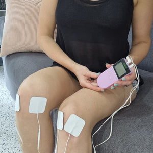 Four white electrode pads placed on a person's thighs with lead wires connected to a handheld Comfee device