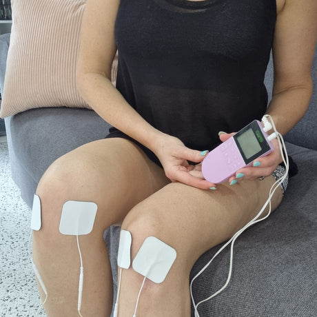Four white electrode pads placed on a person's thighs with lead wires connected to a handheld Comfee device